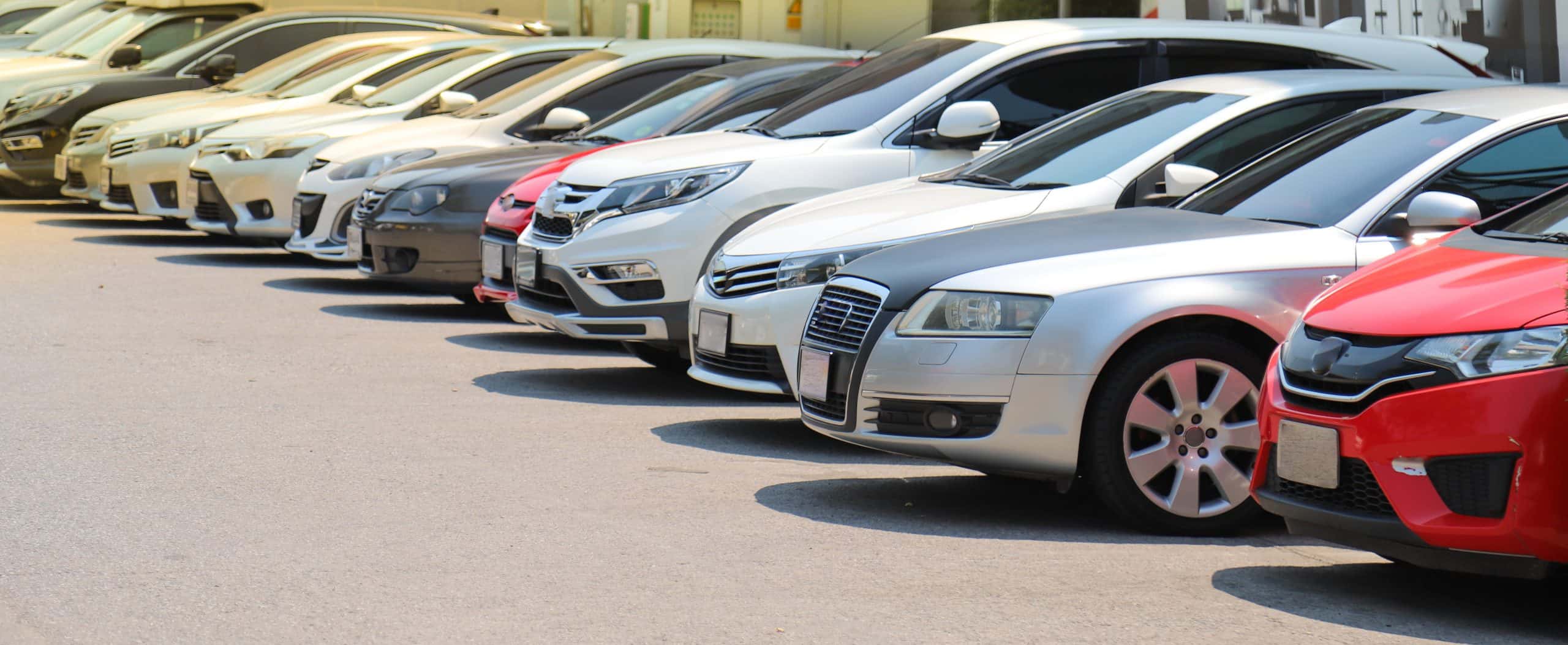 Closeup of front side of cars parking in outdoor parking lot beside the street beside the street in bright sunny day.