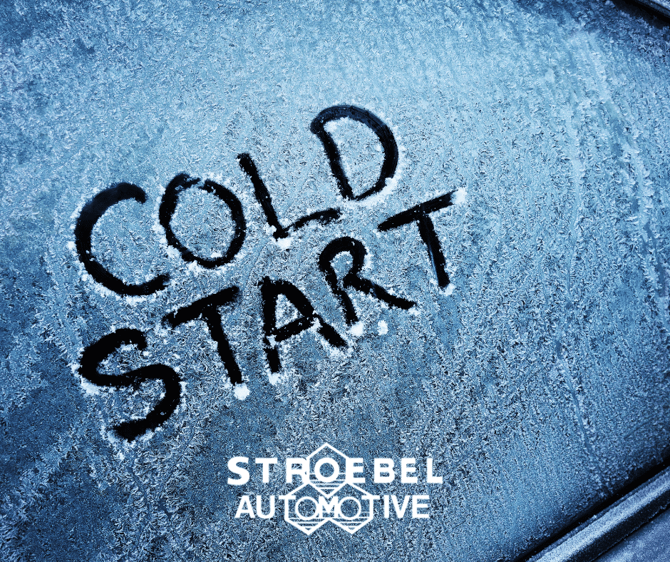 Frosted car window with "Cold Start" message written in snow, ice-covered vehicle surface.